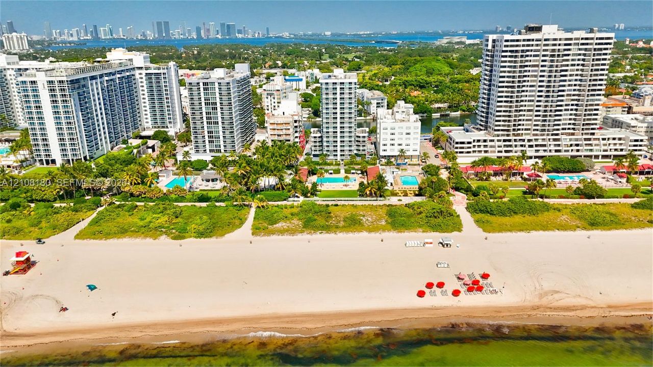 Aerial perspective of oceanfront property featuring sandy beach access, mature tropical landscaping, and outdoor swimming pools