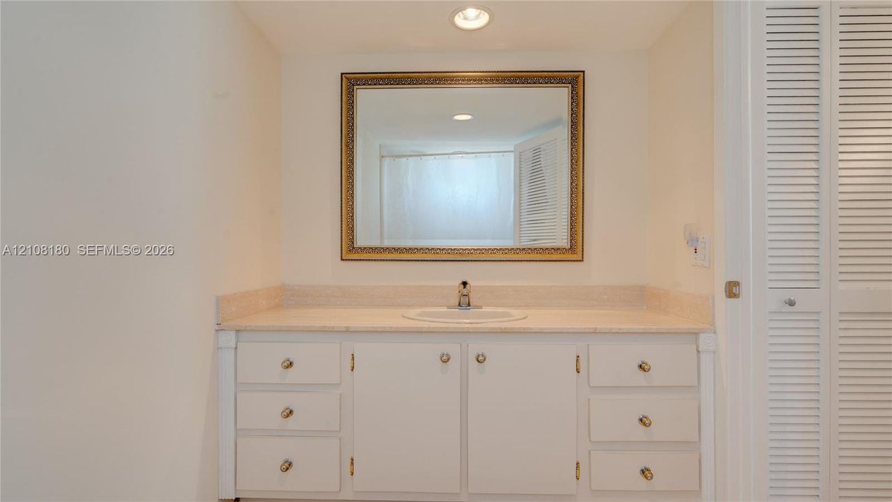Vanity featuring a stone countertop, integrated sink, white cabinetry with metallic hardware, and a framed wall-mounted mirror