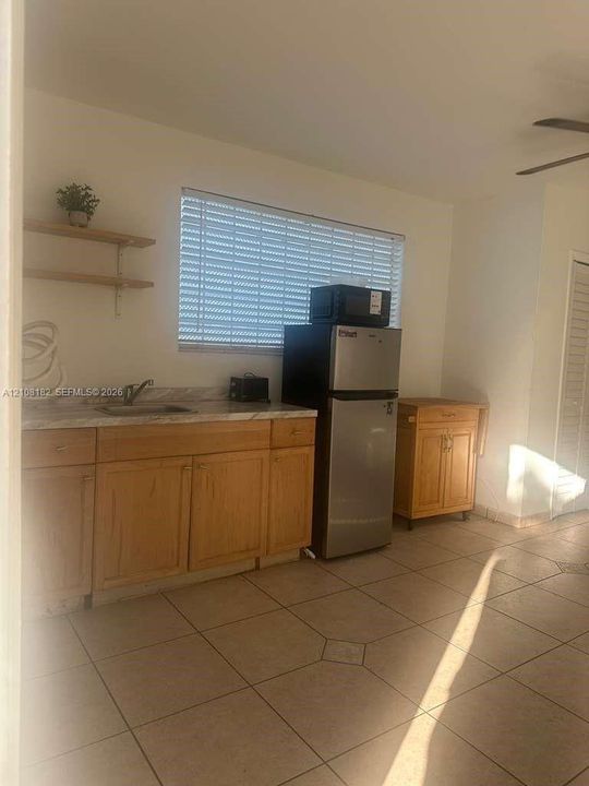 Kitchenette featuring wood cabinetry, stone-finish countertops, stainless steel sink with a metallic faucet, and ceramic tile flooring