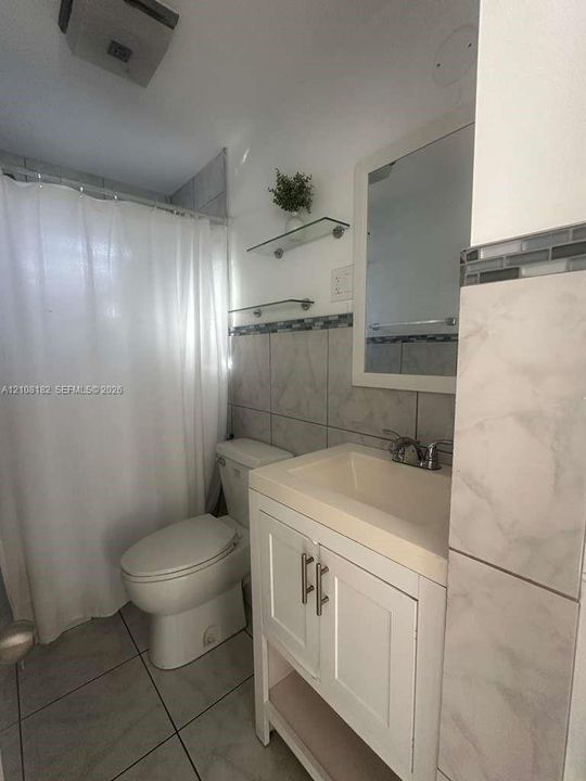 Bathroom featuring a white vanity cabinet with a stone-surface countertop, metal hardware, glass wall-mounted shelving, and tiled wall accents