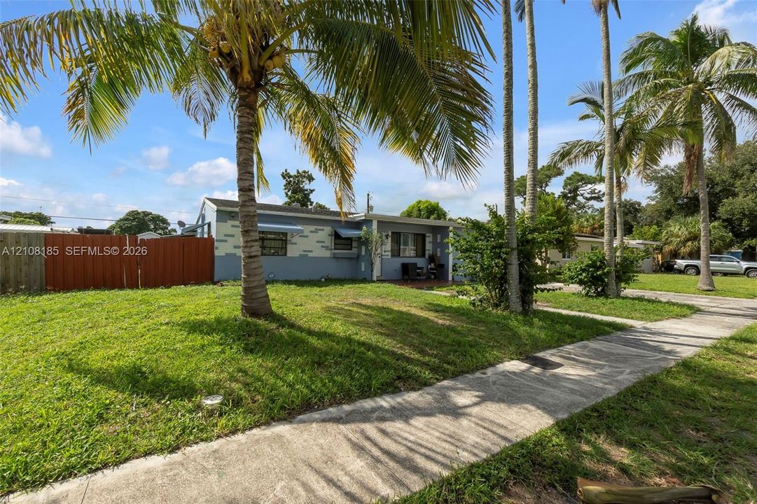 Exterior facade featuring painted masonry, horizontal siding, mature palm trees, a concrete walkway, and a privacy fence