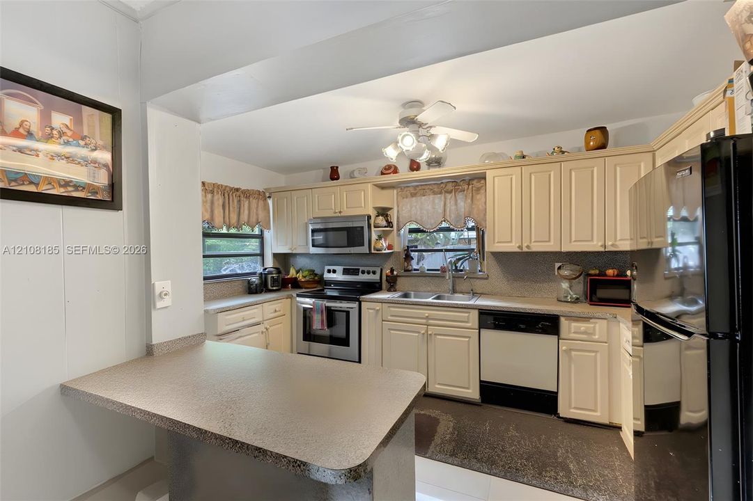 Kitchen featuring shaker-style cabinetry, an integrated breakfast bar, stainless steel appliances, a dual-basin sink, and a ceiling-mounted light fixture