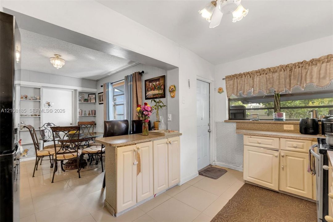 Kitchen featuring light-toned cabinetry, solid surface countertops, built-in shelving, tile flooring, and overhead lighting fixtures