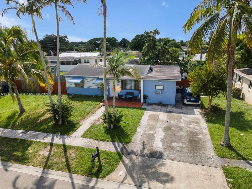 Single-story residence featuring a painted masonry exterior, covered front porch with tiled flooring, concrete driveway, and mature palm trees situated on a grassy lot