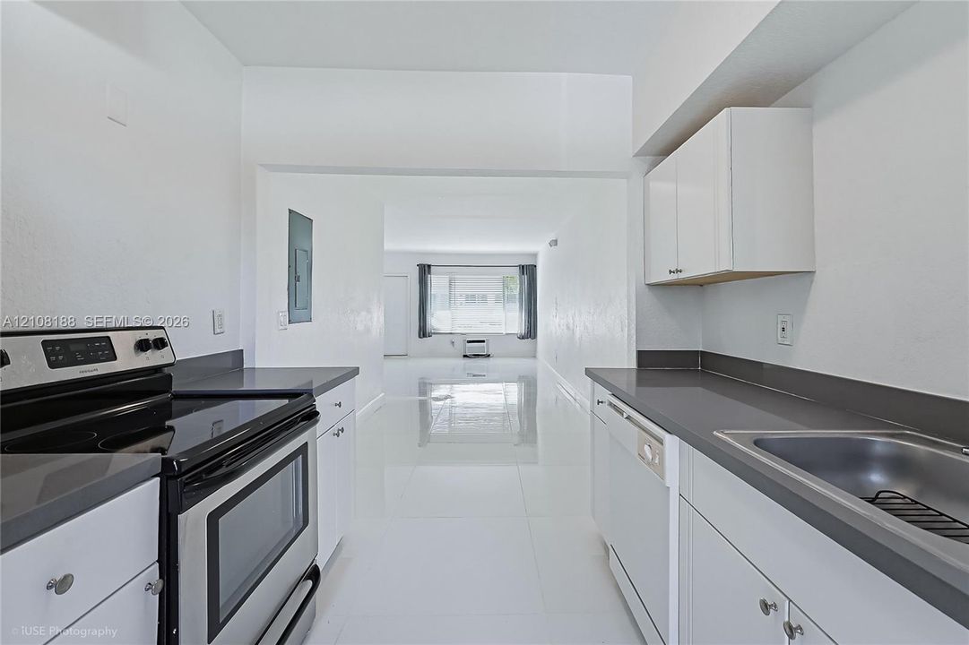Kitchen featuring white cabinetry, solid-surface countertops, stainless steel electric range, built-in dishwasher, and large-format tile flooring