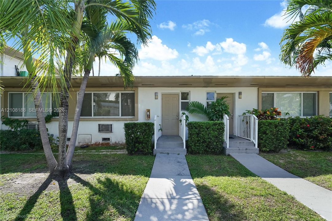 Single-story exterior featuring a light-toned stucco facade, dual entry points with concrete steps, metal handrails, and mature palm trees