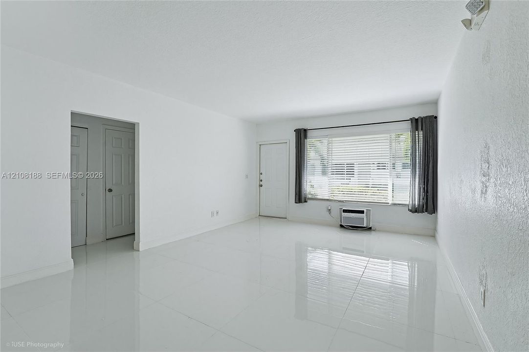 Bright interior space featuring polished tile flooring, a large picture window with horizontal blinds, and a wall-mounted air conditioning unit