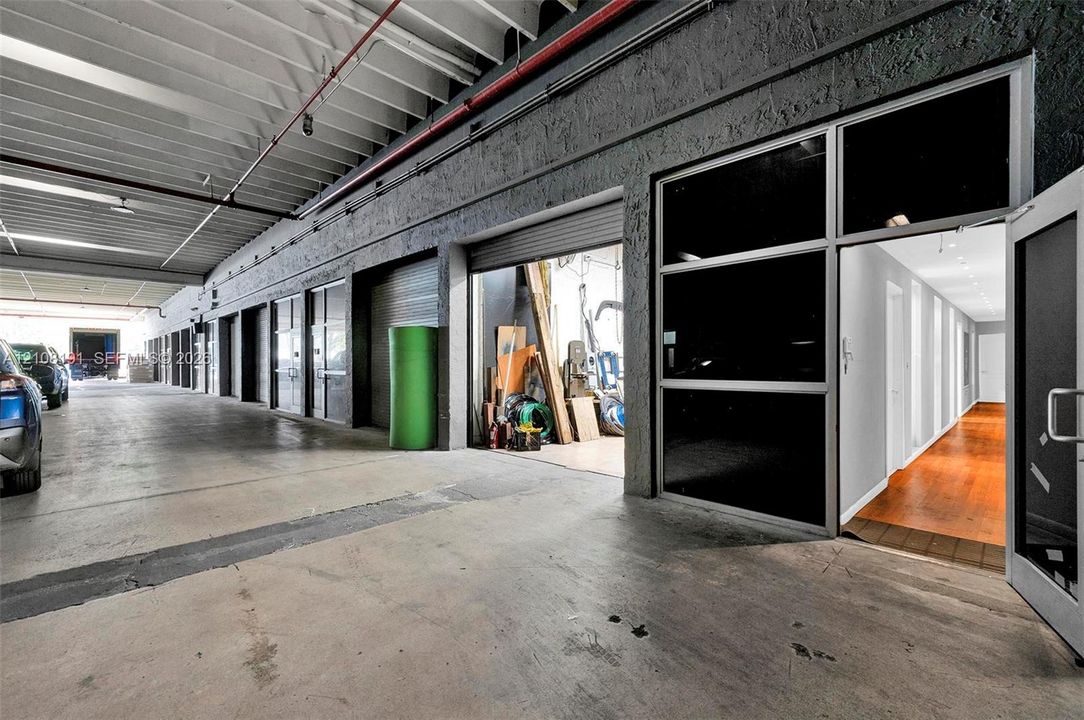 Industrial space featuring a concrete floor, high exposed-beam ceilings, roll-up metal bay door, and glass-paneled entry doors