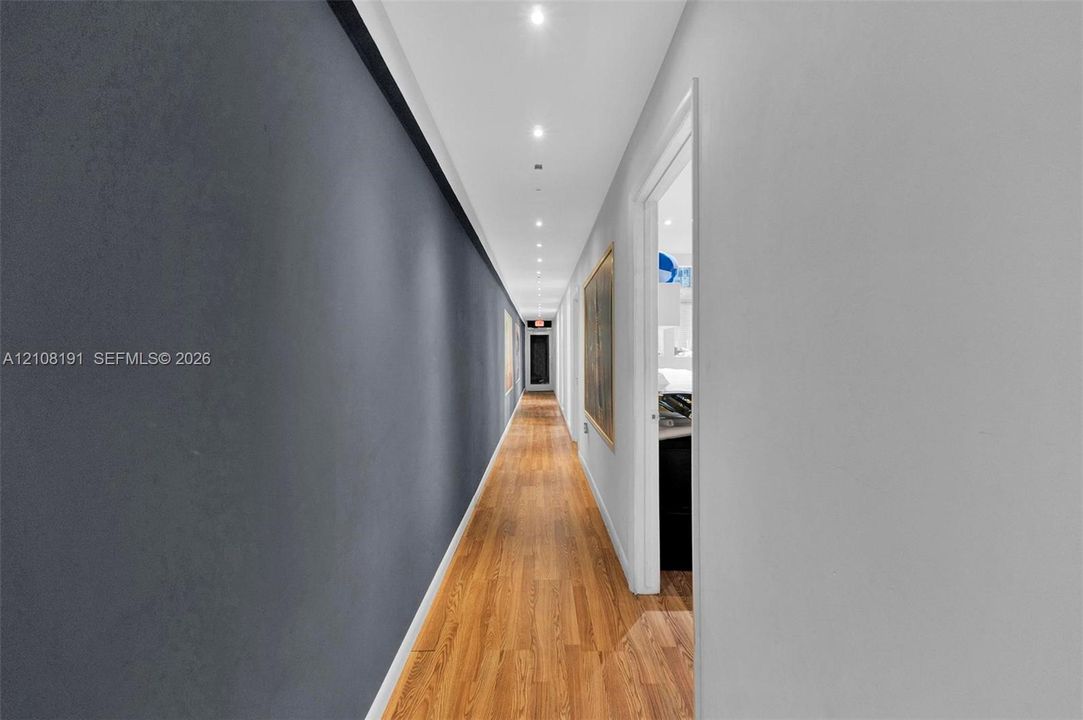 Hallway featuring wood-finish flooring, charcoal-toned accent wall, crisp white walls, and recessed ceiling lighting