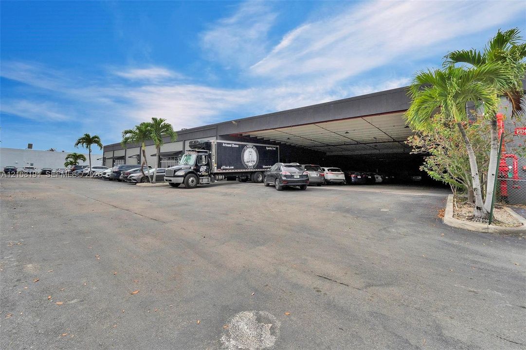 Commercial facility featuring an expansive paved exterior parking area, a recessed covered loading dock, and established palm landscaping