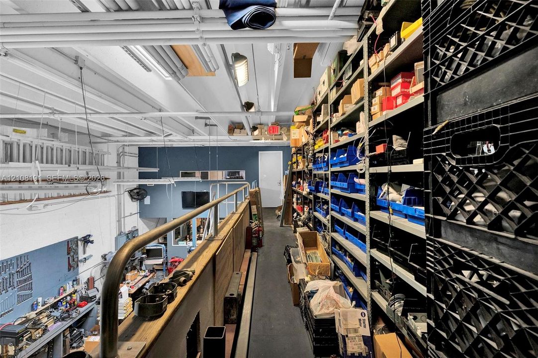 Industrial mezzanine level featuring metal safety railings, exposed ceiling infrastructure, and extensive built-in industrial steel shelving units