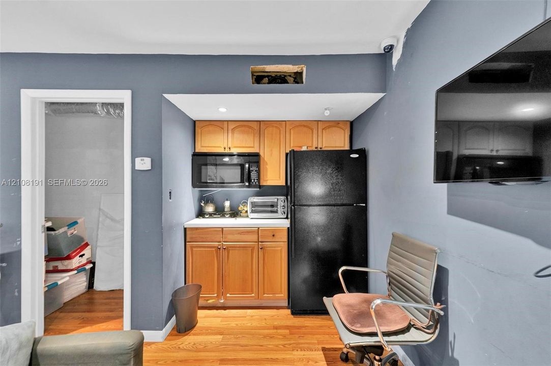 Kitchenette featuring light wood cabinetry, stone-finish countertops, and black appliances including a refrigerator and built-in microwave, complemented by wood-finish flooring