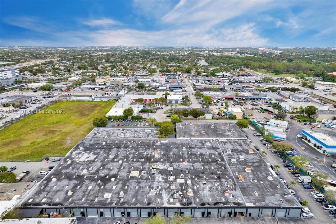 Industrial facility featuring a large-scale flat roof, multiple overhead bay doors, paved surface parking, and direct street access