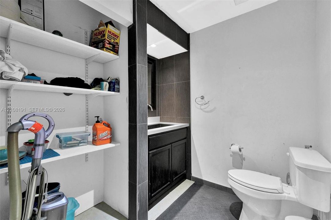 Bathroom featuring a vanity with dark cabinetry and a light-toned countertop, dark tile wall surround, and wall-mounted shelving unit
