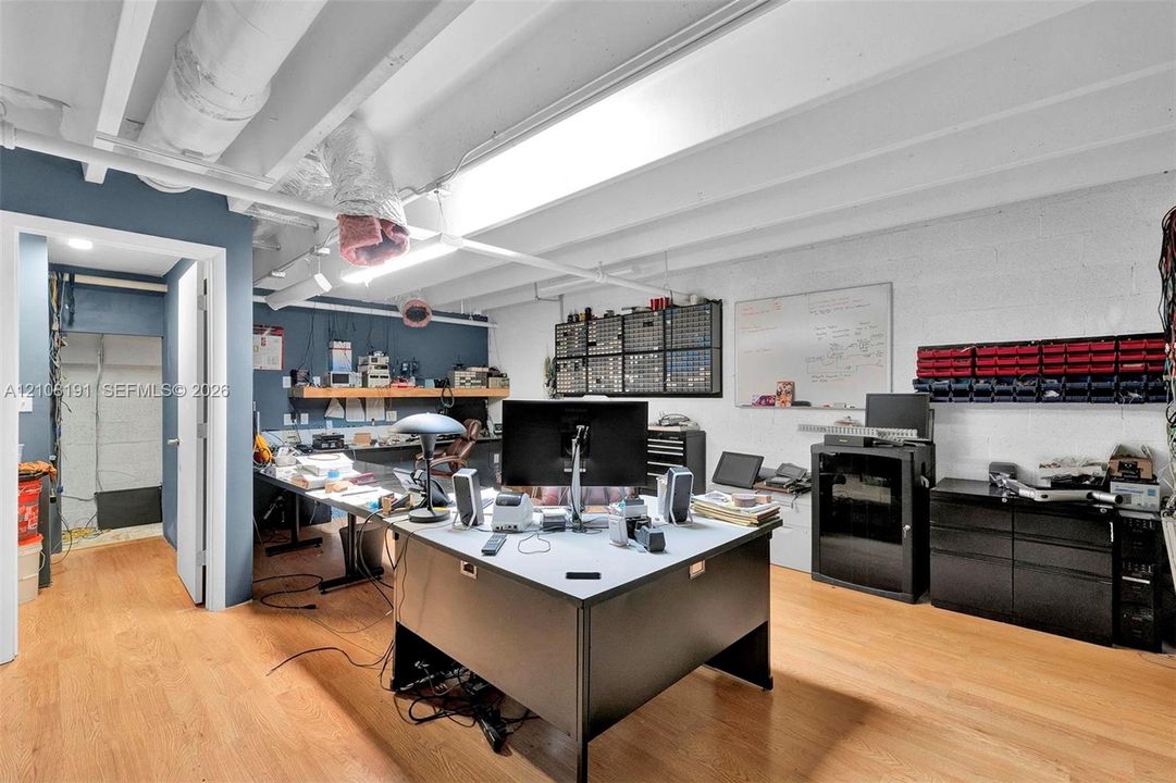 Open-concept workspace featuring wood-finish flooring, exposed structural ceiling beams, and built-in wall storage shelving