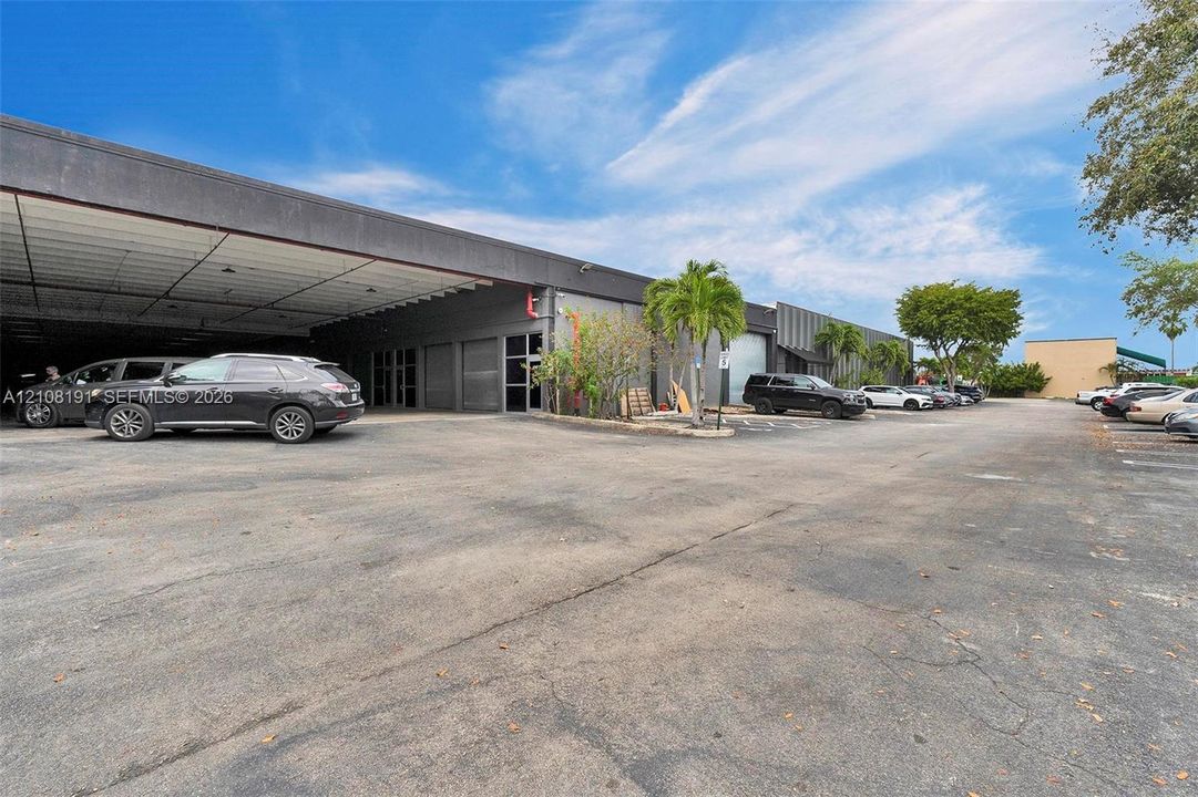 Commercial exterior featuring a concrete facade, expansive covered parking area, multi-bay entry points, and paved surface lot