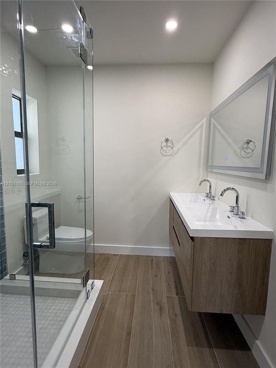 Floating vanity featuring a dual-sink integrated basin, wood-finish cabinetry, porcelain tile flooring, and a glass-enclosed shower with a modern chrome-finish hardware suite