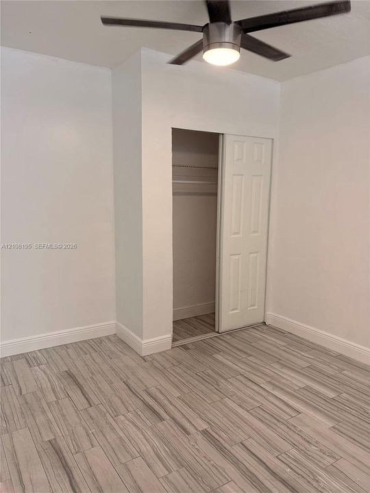 Room featuring wood-finish tile flooring, a neutral color palette, a ceiling fan with integrated lighting, and a closet with a paneled sliding door