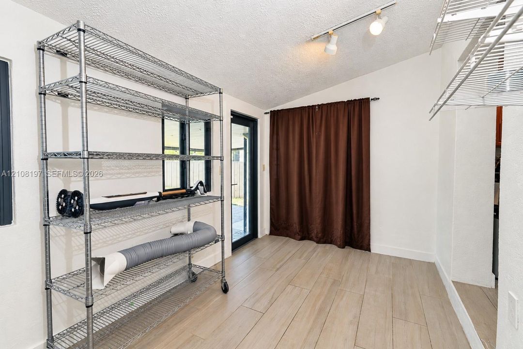 Wood-finish tile flooring, vaulted ceiling, multi-light track lighting, and a glass-paneled exterior door