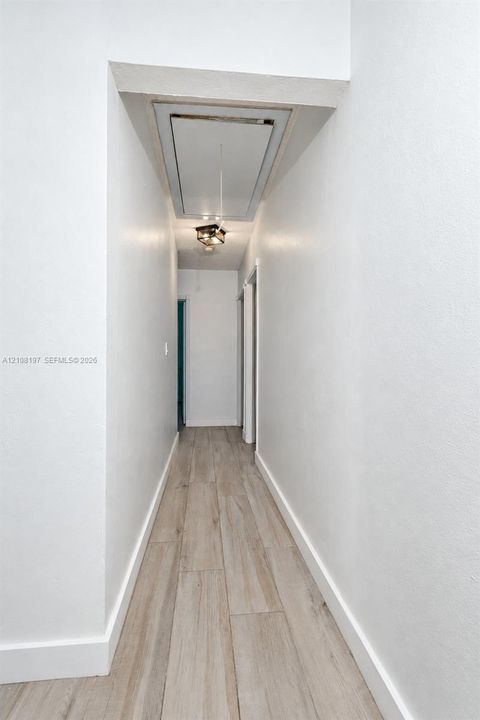 Hallway featuring wood-finish flooring, smooth-finish walls, and a recessed ceiling access panel with an integrated light fixture