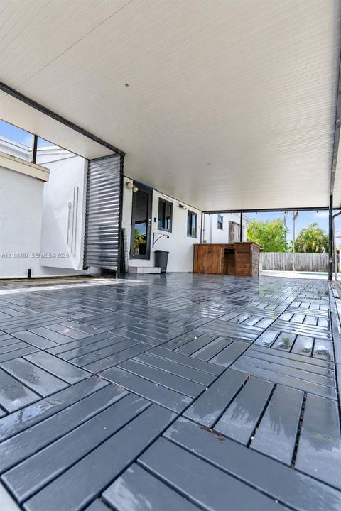 Covered patio featuring gray interlocking deck tiles, white ceiling paneling, and a built-in wooden structure