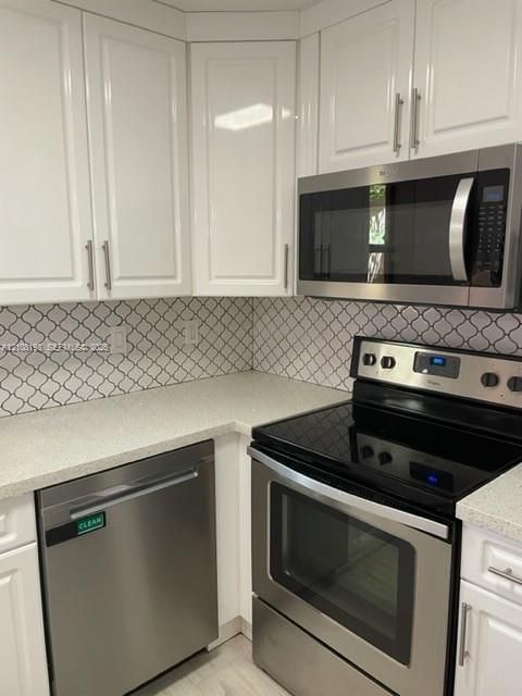 Kitchen featuring white cabinetry with brushed-metal pulls, stainless steel appliances, patterned tile backsplash, and stone-finish countertops
