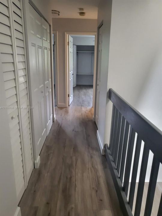 Hallway featuring wood-finish flooring, white louvered bi-fold closet doors, and a dark-toned vertical slat railing