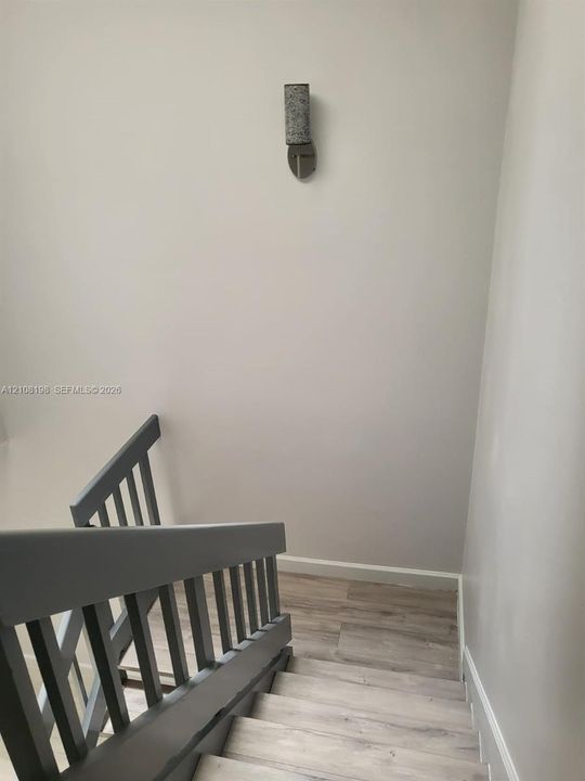 Staircase featuring wood-finish flooring, a painted wooden balustrade, and a cylindrical wall-mounted light fixture