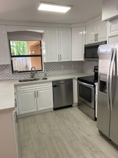 Kitchen featuring white shaker-style cabinetry, stainless steel appliances, patterned tile backsplash, quartz countertops, and wood-finish flooring