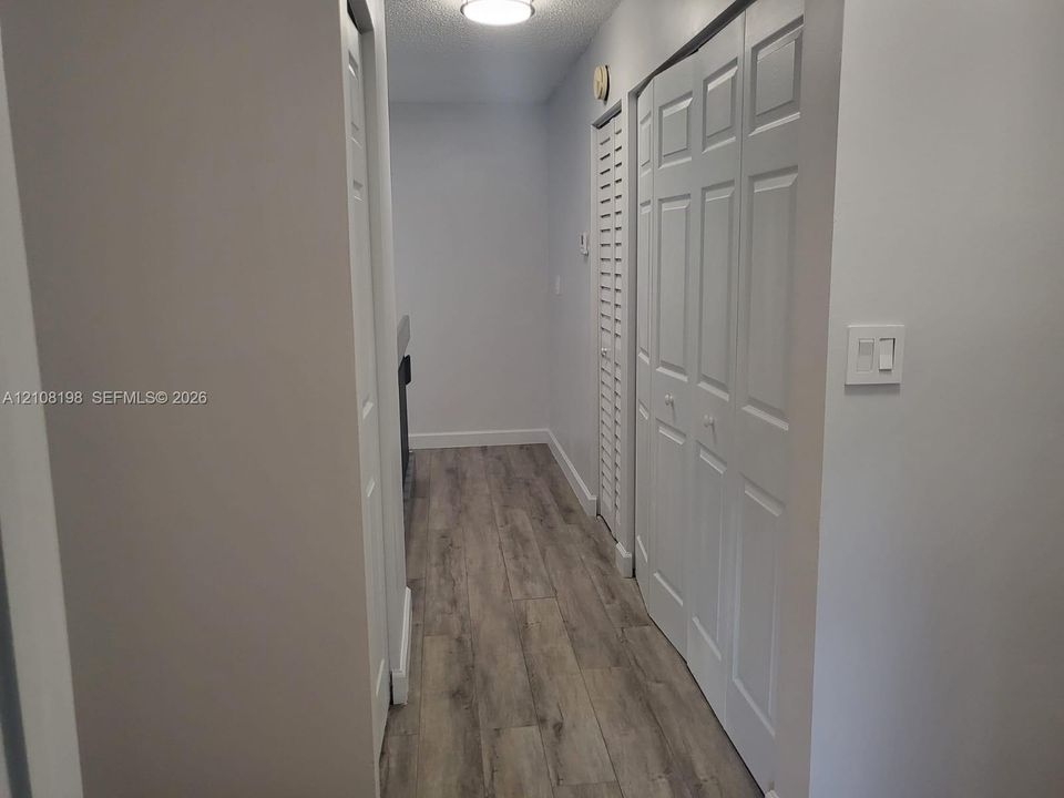 Hallway featuring wood-finish flooring, two sets of white paneled bifold closet doors, and flush-mount overhead lighting