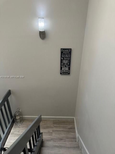 Staircase featuring wood-finish flooring, a metal-railed banister, and a brushed-nickel wall-mounted light fixture with a textured glass shade