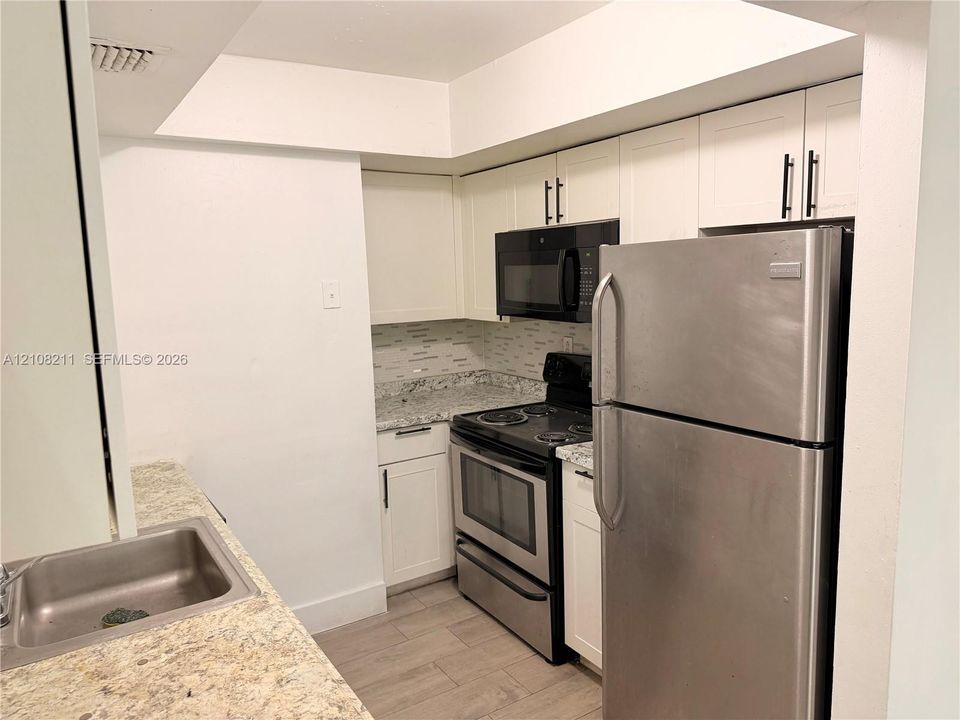 Kitchen featuring white cabinetry with matte black hardware, stone-patterned countertops, stainless steel appliances, a tile backsplash, and wood-finish flooring