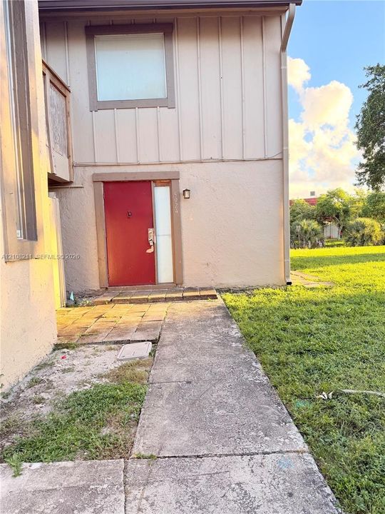 Exterior featuring vertical board-and-batten siding, stucco finish, a red entry door with sidelight, and a concrete paver walkway