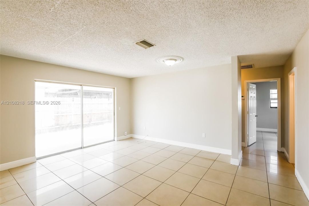 Neutral-toned interior space featuring light-colored ceramic tile flooring, sliding glass doors, a ceiling-mounted light fixture with medallion detail, and textured ceiling finish