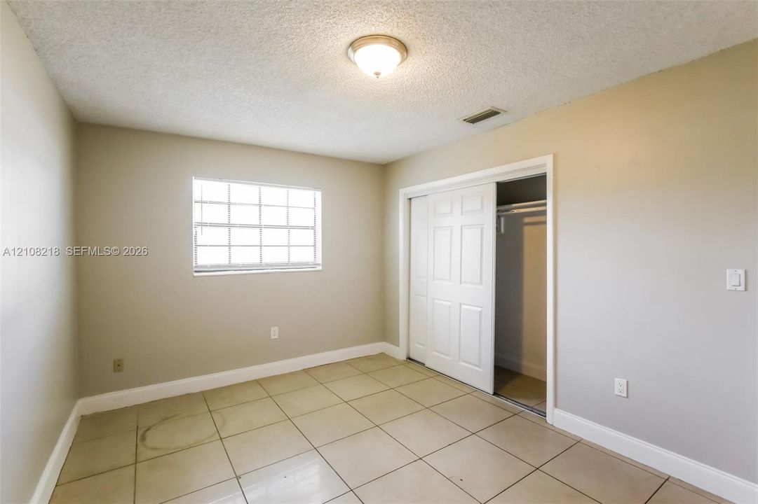 Neutral-toned room featuring large-format square tile flooring, a multi-pane window, and a built-in closet with white paneled sliding doors