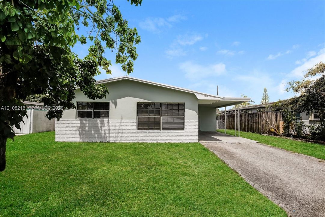 Single-story exterior featuring a painted brick facade, low-pitch roofline, attached carport, and a paved driveway