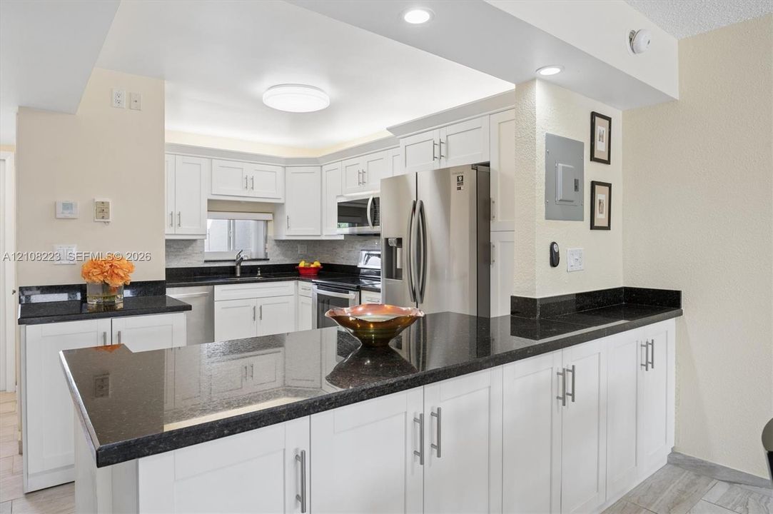 Kitchen featuring white shaker-style cabinetry, dark stone countertops, stainless steel appliances, recessed ceiling lighting, and a breakfast bar
