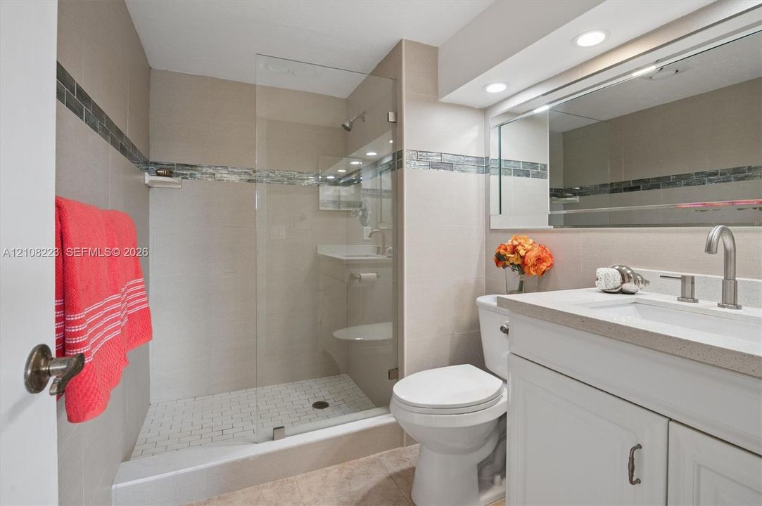 Bathroom featuring a walk-in glass-enclosed shower, mosaic tile wall accent, white vanity cabinet with a solid surface countertop, and integrated recessed lighting