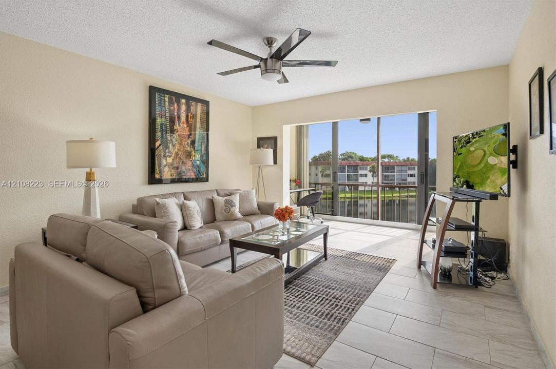 Living area featuring large-format tile flooring, a central multi-blade ceiling fan, and floor-to-ceiling sliding glass doors opening to a screened balcony