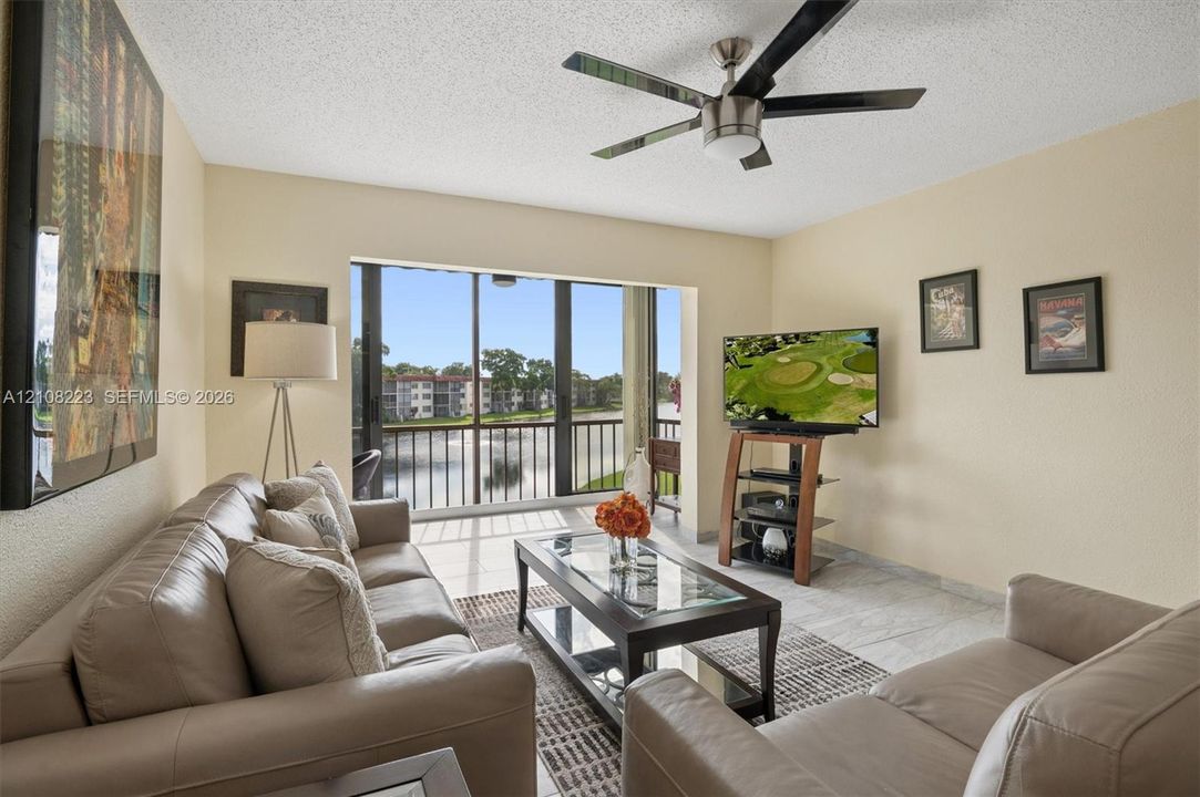 Living area featuring large format tile flooring, a multi-blade ceiling fan, and floor-to-ceiling glass sliding doors opening to a railed balcony