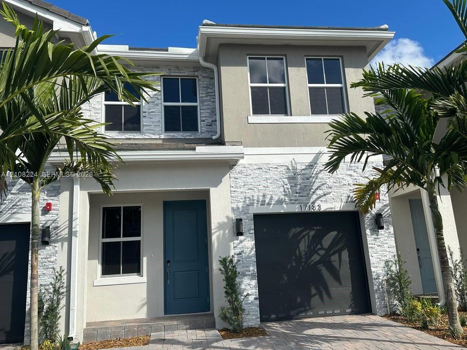 Two-story exterior featuring a stone veneer facade, integrated single-car garage, multi-pane windows, and a covered entryway with a solid-panel door