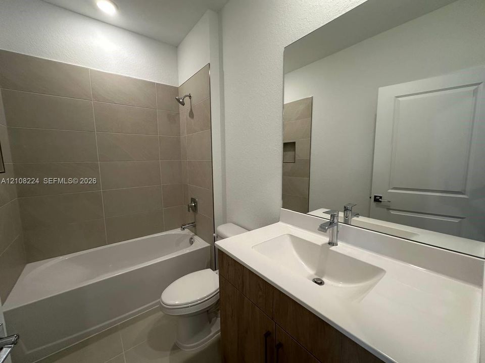 Bathroom featuring a vanity with a white integrated sink, wood-finish cabinetry, a large wall-mounted mirror, and a tiled shower-tub combination