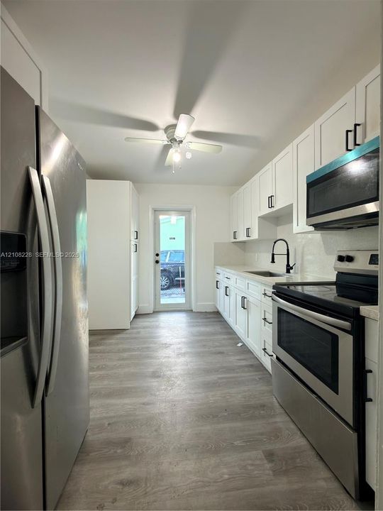 Kitchen featuring white cabinetry with matte black hardware, stainless steel appliances, wood-finish flooring, a matte black kitchen faucet, and a ceiling-mounted light fixture