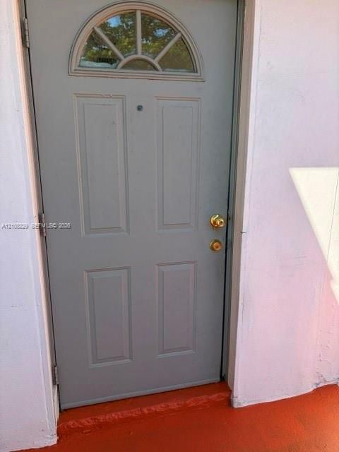 Gray four-panel door featuring a semi-circular transom window, brass-finish hardware, and a door viewer