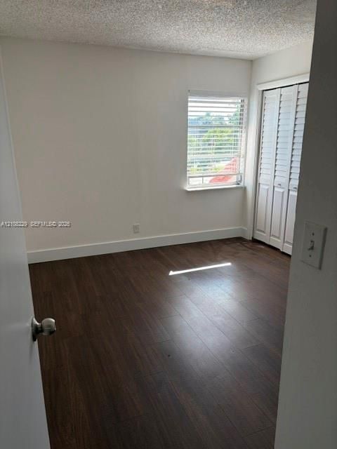 Room featuring wood-finish flooring, white walls, and a window with horizontal blinds, complemented by white bi-fold closet doors
