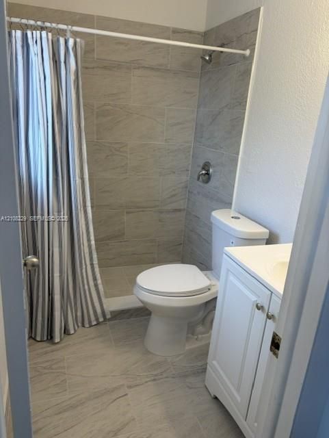 Bathroom featuring large-format tile flooring, a shower surround with neutral tile detailing, a white vanity cabinet, and a two-piece toilet