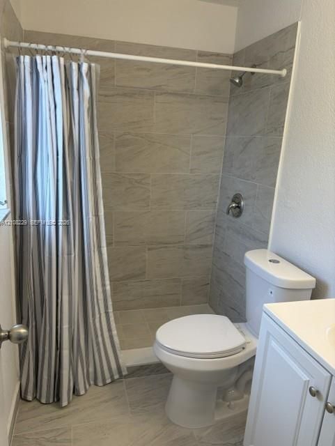 Full-height ceramic tile shower surround, porcelain floor tile, white vanity cabinet, dual-flush toilet, and wall-mounted shower fixture