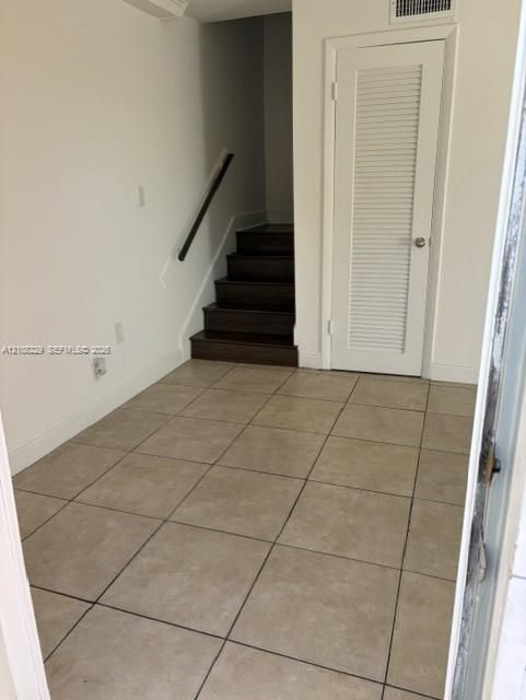 Neutral-toned tile flooring, dark wood-finish staircase, and louvered-panel closet door