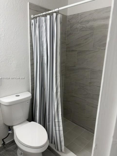 Shower enclosure featuring floor-to-ceiling large-format neutral-toned tile work and a white porcelain commode