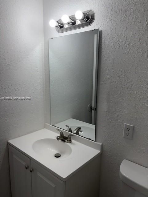 Bathroom vanity featuring a solid-surface countertop with an integrated basin, white cabinetry, polished metal faucet, wall-mounted mirror, and a three-light fixture